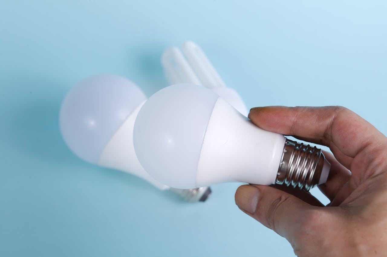 why-choose-us Close-up of hand holding energy-efficient LED light bulbs on a blue background.